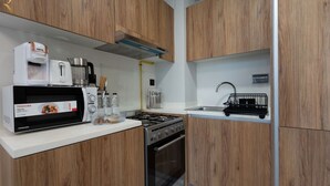 A compact kitchen with wooden cabinets, a microwave, a stove, and a sink. - Modern 1BR w/ Balcony | Maryah Vista Retreat (Abu Dhabi)