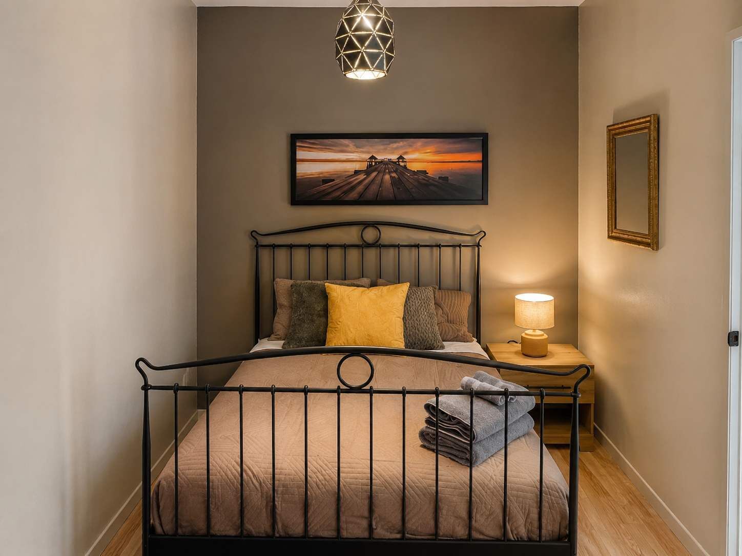 Un lit avec un cadre en métal, une lampe de chevet, un tableau encadré au mur et un miroir accroché au mur.