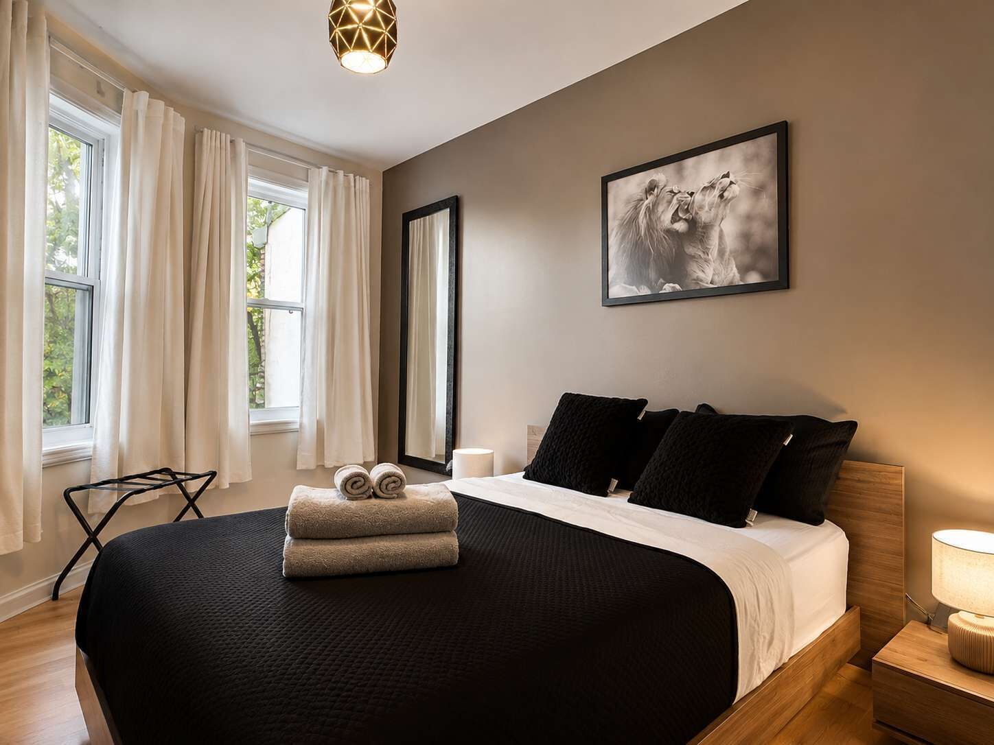 Ein Schlafzimmer mit Bett, einem großen Fenster, einem Gemälde und einem Nachttisch mit Lampe.