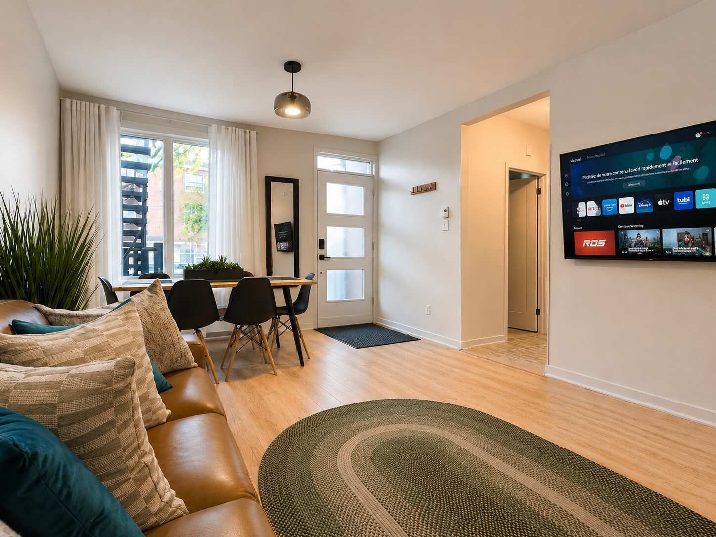 Ein modernes Wohnzimmer mit einer Couch, einem Essbereich und einem Fernseher, der eine Streaming-Oberfläche zeigt.