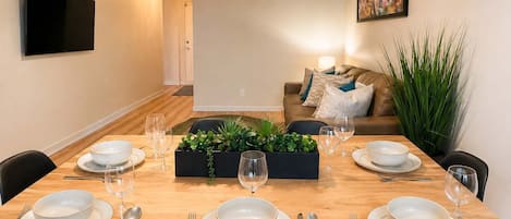 A dining area with a wooden table set for four, surrounded by chairs.
