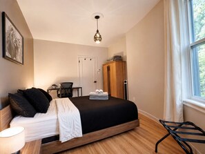 A bedroom with a bed, bedside table, lamp, chair, wardrobe, and a window. - Limoilou | EV Charger | Parking | The 570 (Québec City)