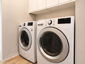 Two front-loading washing machines in a laundry room with a wooden floor and white walls. - Limoilou | EV Charger | Parking | The 570 (Québec City)