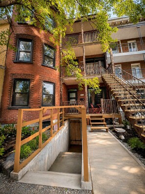 A multi-story building with a brick facade, wooden staircases, and a small outdoor seating area. - Limoilou | EV Charger | Parking | The 570 (Québec City)