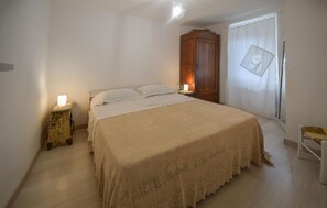 Ein Schlafzimmer mit einem großen Bett, einem Holzschrank, einem Nachttisch mit Lampe und einem Fenster mit Vorhang.