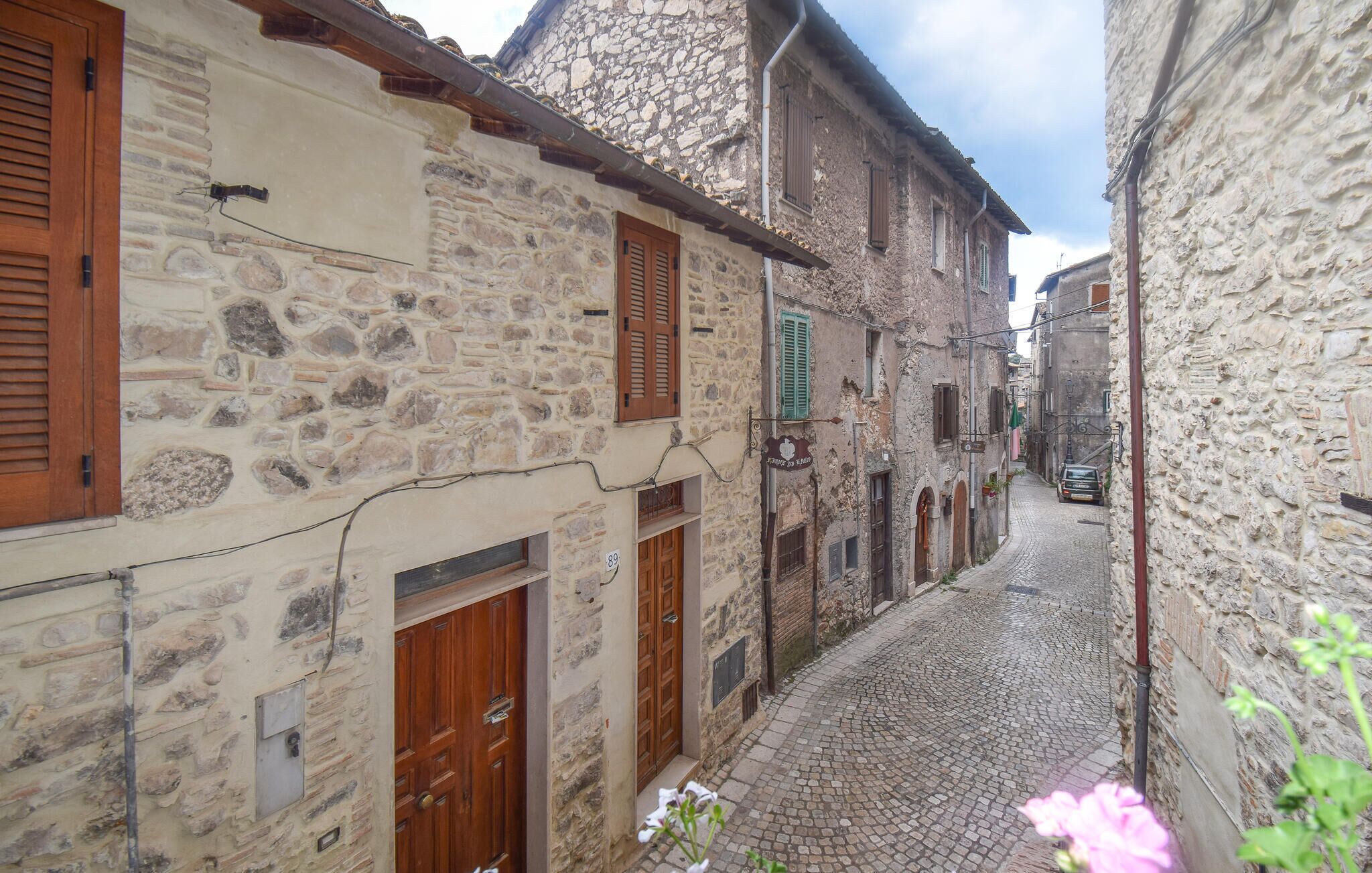A narrow cobblestone street flanked by stone buildings with wooden shutters and doors.