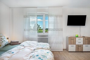 Un dormitorio con cama, un radiador, un televisor montado en la pared y un mueble de madera con cajones.