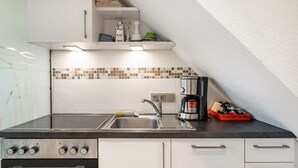 Ett kök med en diskho i rostfritt stål, en kaffebryggare och ett diskställ.