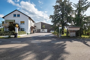 Ein zweistöckiges Gebäude mit flachem Dach und einem großen Baum davor.