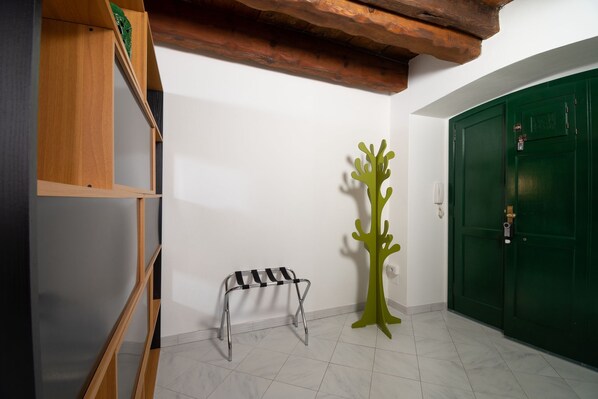A room with a green door, a wooden shelf, a metal bench, and a green abstract sculpture.