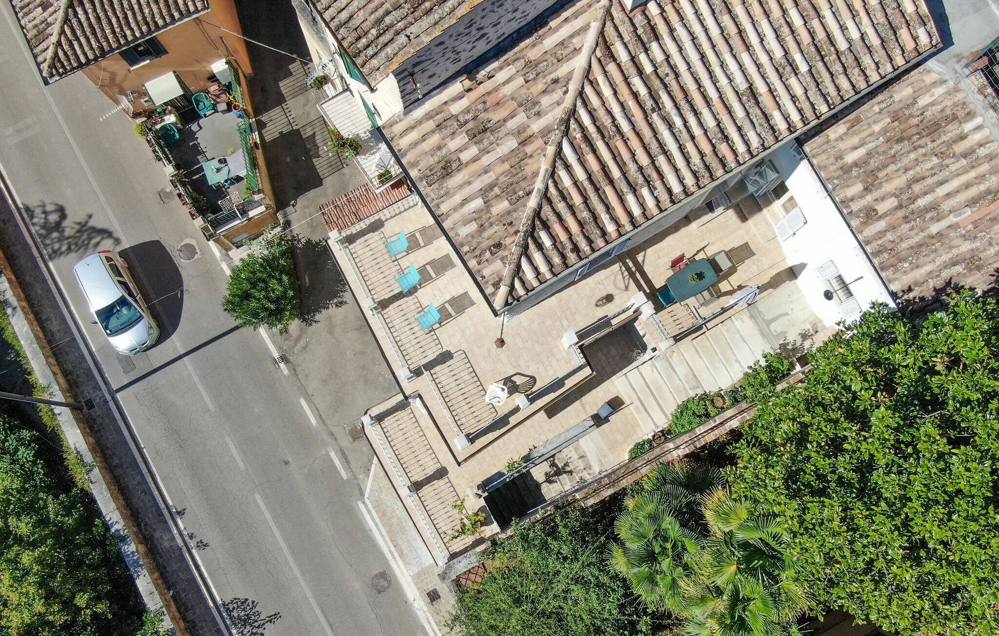 Vue aérienne d’un quartier résidentiel avec des toits recouverts de tuiles en terre cuite, une rue bordée de voitures garées et de verdure.