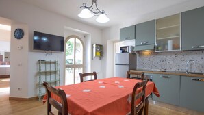 Uma sala de jantar com uma mesa posta para quatro pessoas, uma cozinha equipada com micro-ondas e frigorífico, e uma televisão fixada na parede.