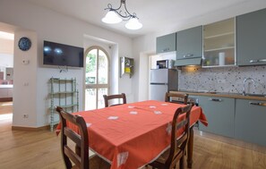 A dining area with a table set for four, a kitchen with a microwave and refrigerator, and a television mounted on the wall. - 3 bedroom pet friendly home in Arrone (TR) (Arrone (TR))