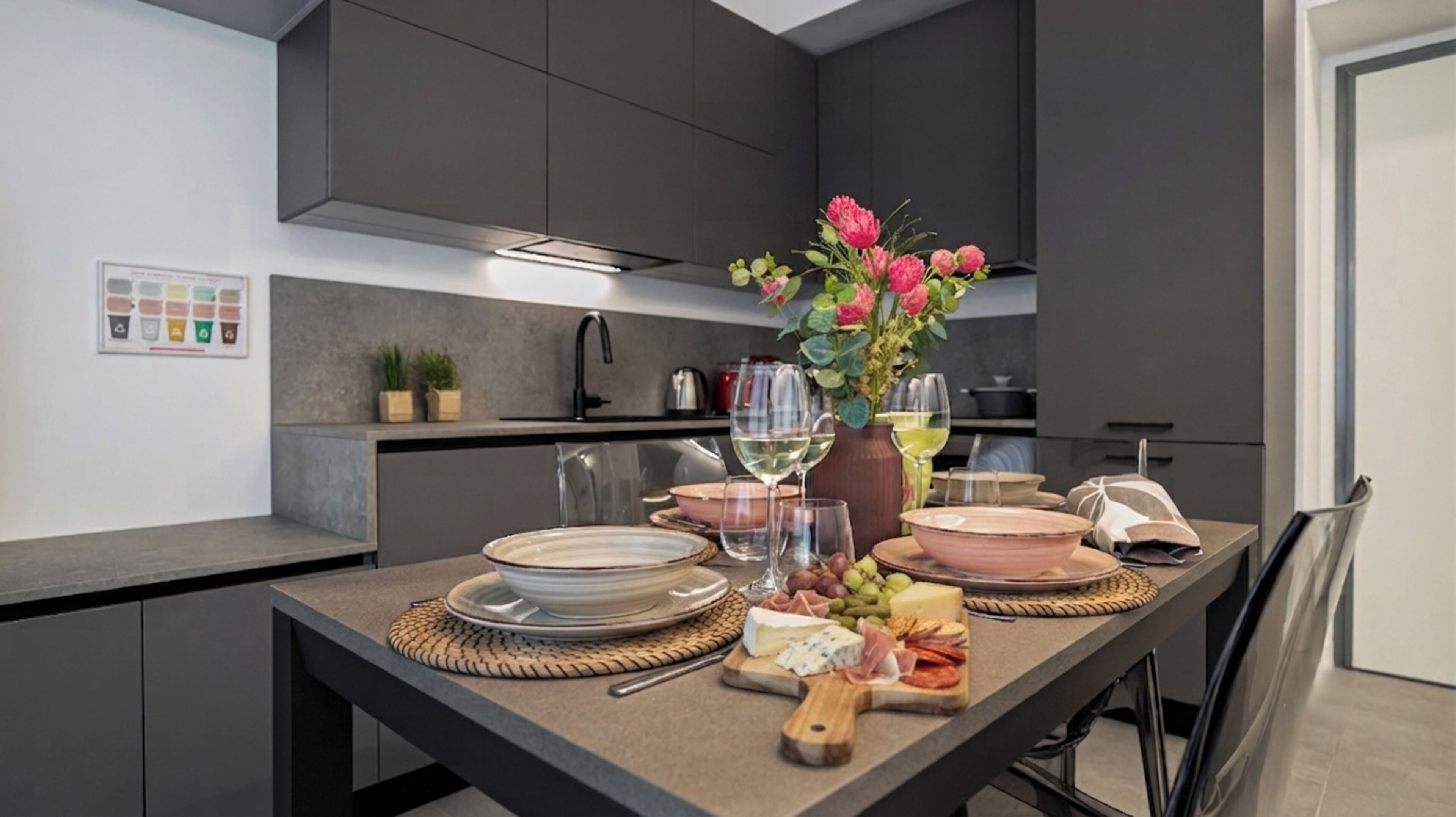 Une cuisine moderne aux meubles sombres, une table à manger dressée avec des assiettes, des verres et un vase de fleurs.