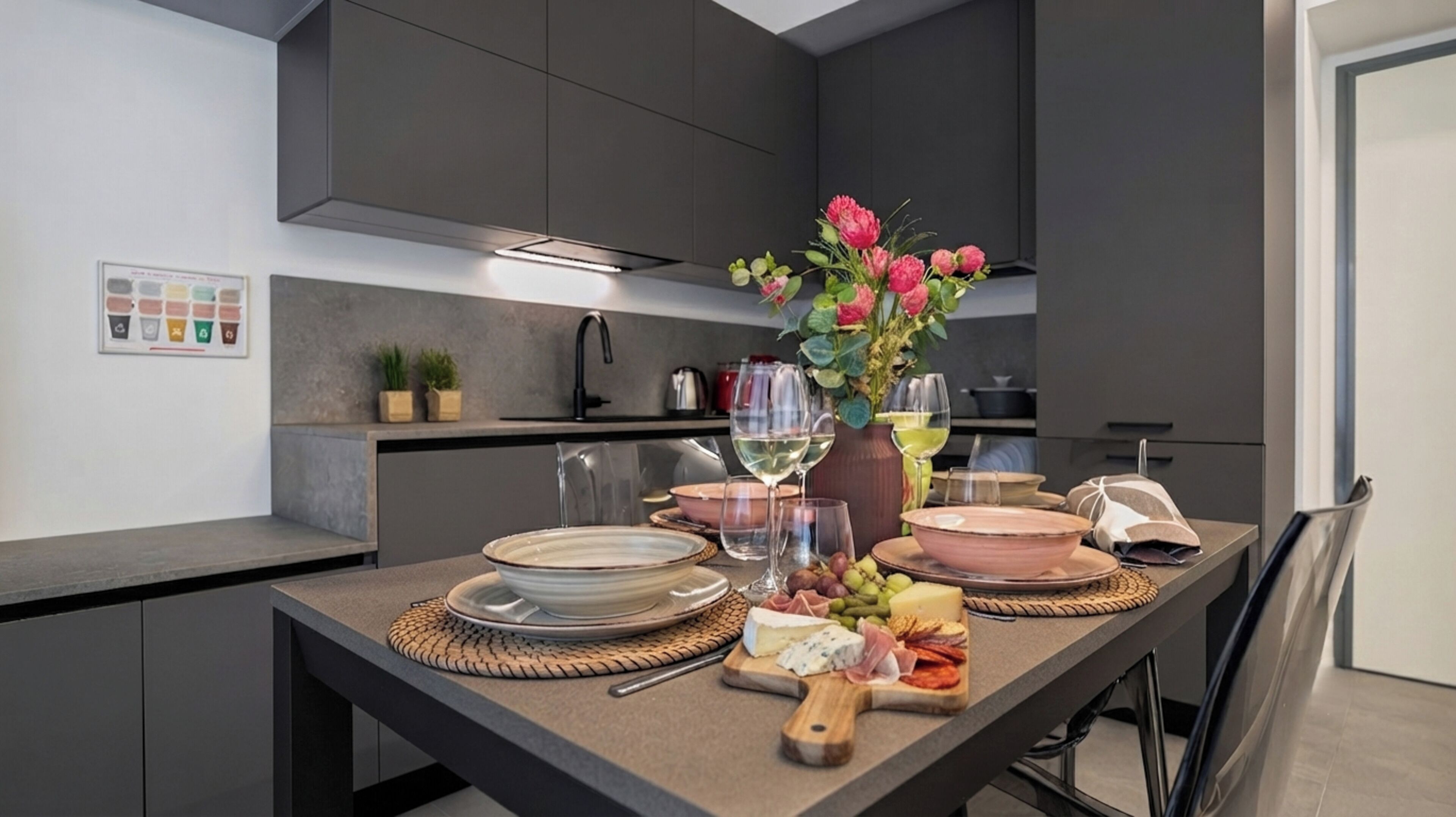 Una cucina moderna con mobili scuri, un tavolo da pranzo apparecchiato con piatti, bicchieri e un vaso di fiori.