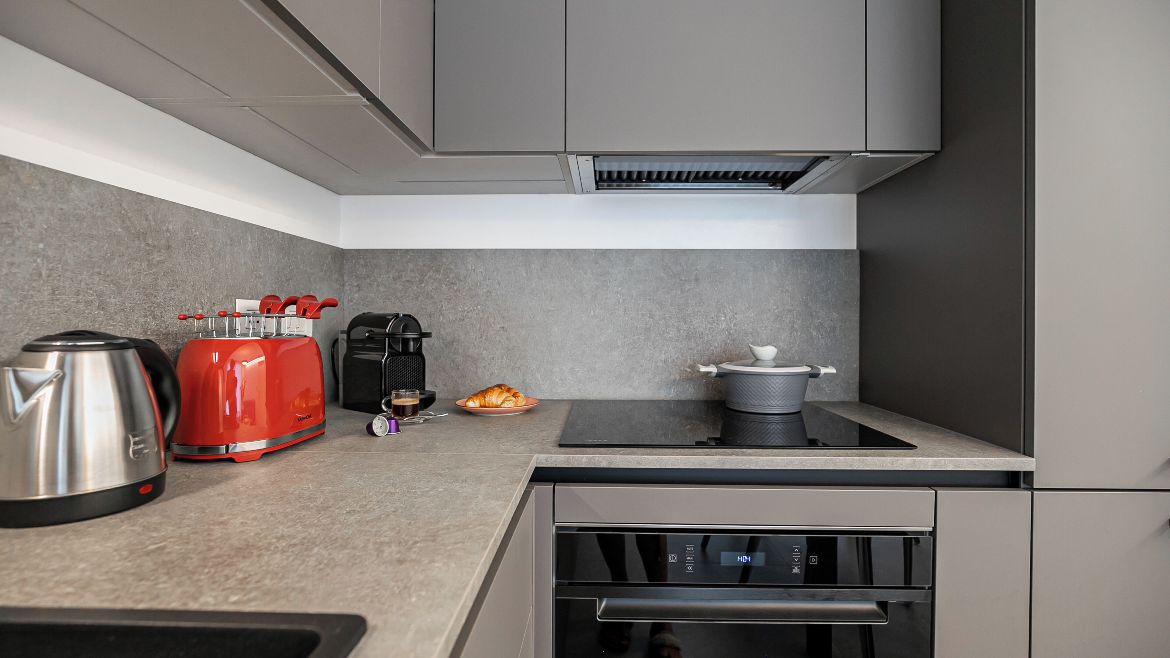 A kitchen with a toaster, coffee maker, kettle, and a pot on the stove.