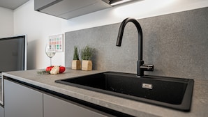 Una cocina con un lavamanos negro, un refrigerador de acero inoxidable y una lámpara fijada a la pared.