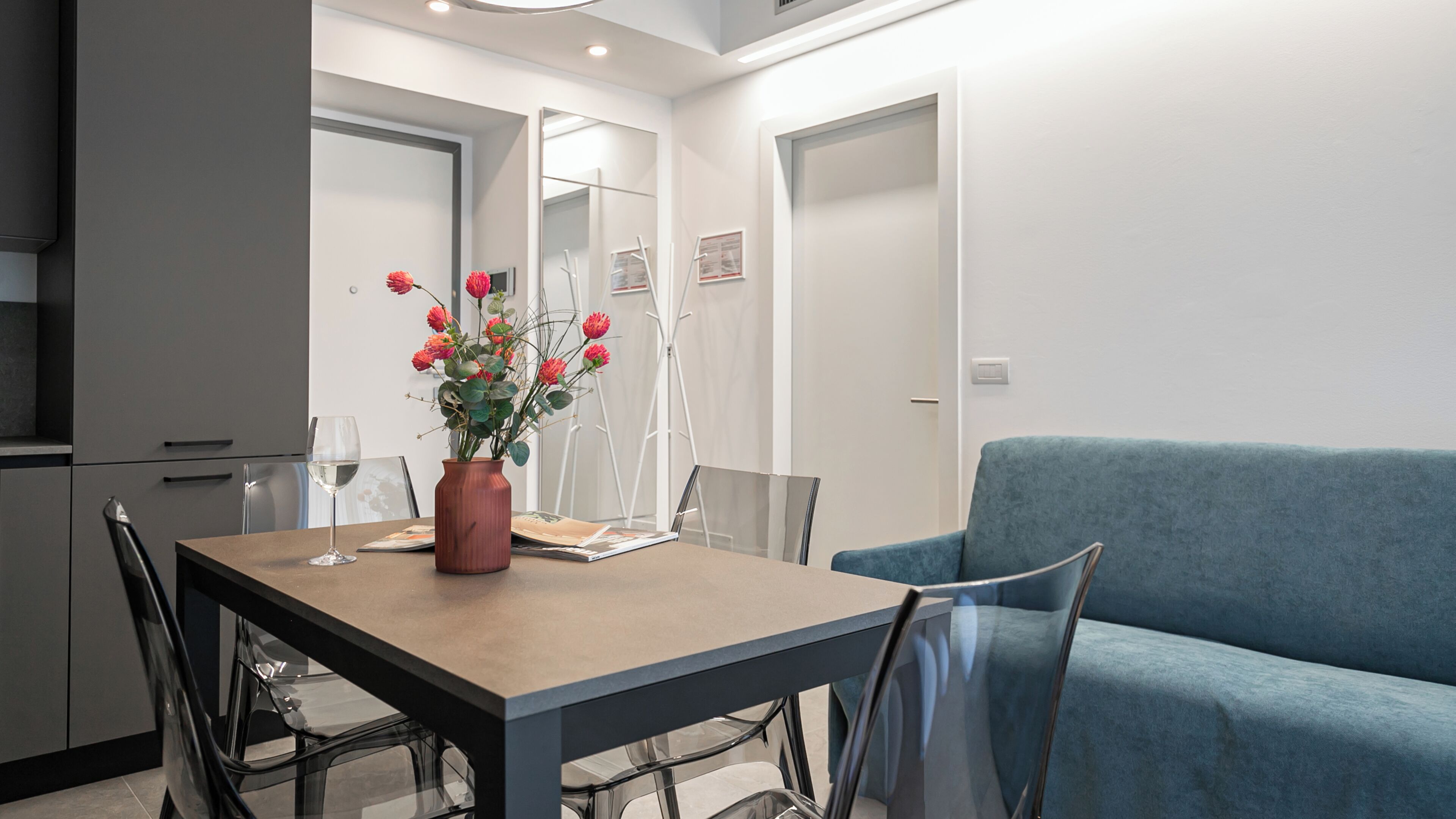 Un comedor moderno con una mesa, sillas, un jarrón de flores y un sofá azul.