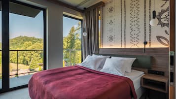 A modern bedroom with a large bed, a view of a forested hillside, and a patterned wall.