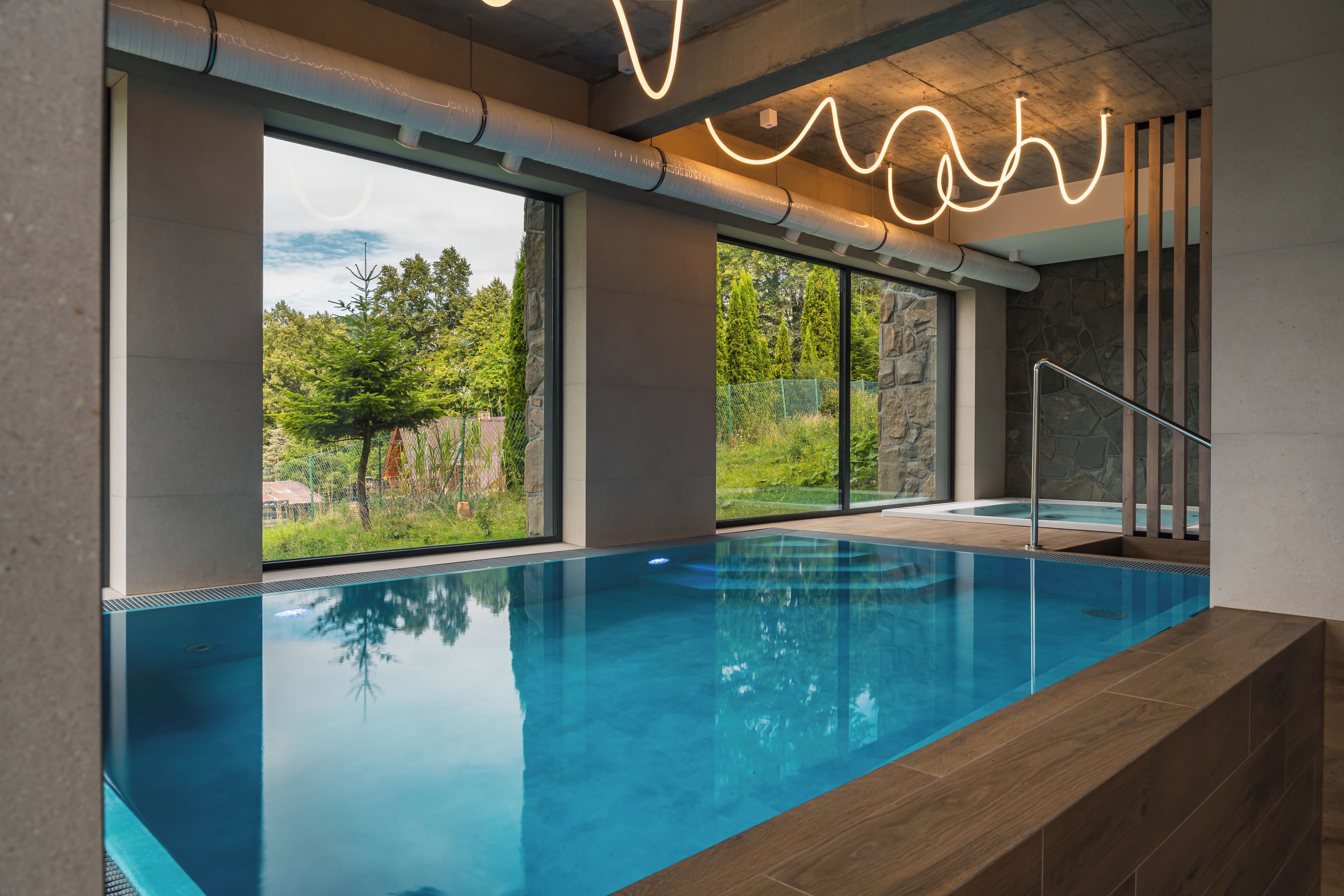 An indoor swimming pool with clear glass walls, a stone wall, and a wooden deck.