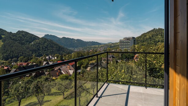 Un balcón con vistas despejadas a un paisaje montañoso, un edificio moderno y una zona residencial.