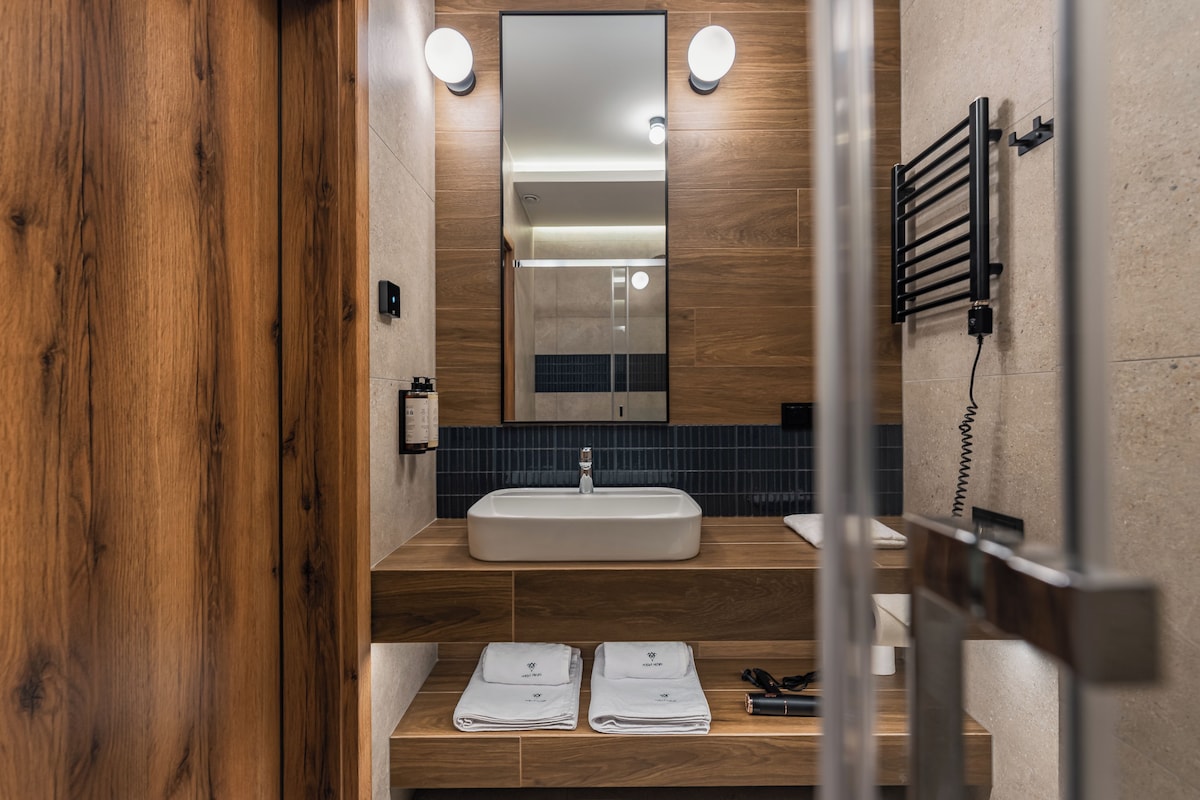Un baño moderno con tocador de madera, un espejo grande, un perchero y un dispensador de toallas.