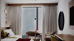 Habitación de hotel con cama, dos sillones, escritorio y un ventanal con cortinas.