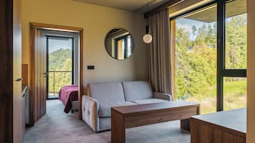 Ein modernes Zimmer mit einer Couch, einem Holztisch und einem großen Fenster mit Blick auf Bäume.