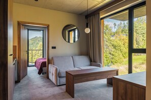Habitación moderna con sofá, una mesa de madera y un ventanal que ofrece vistas a árboles.