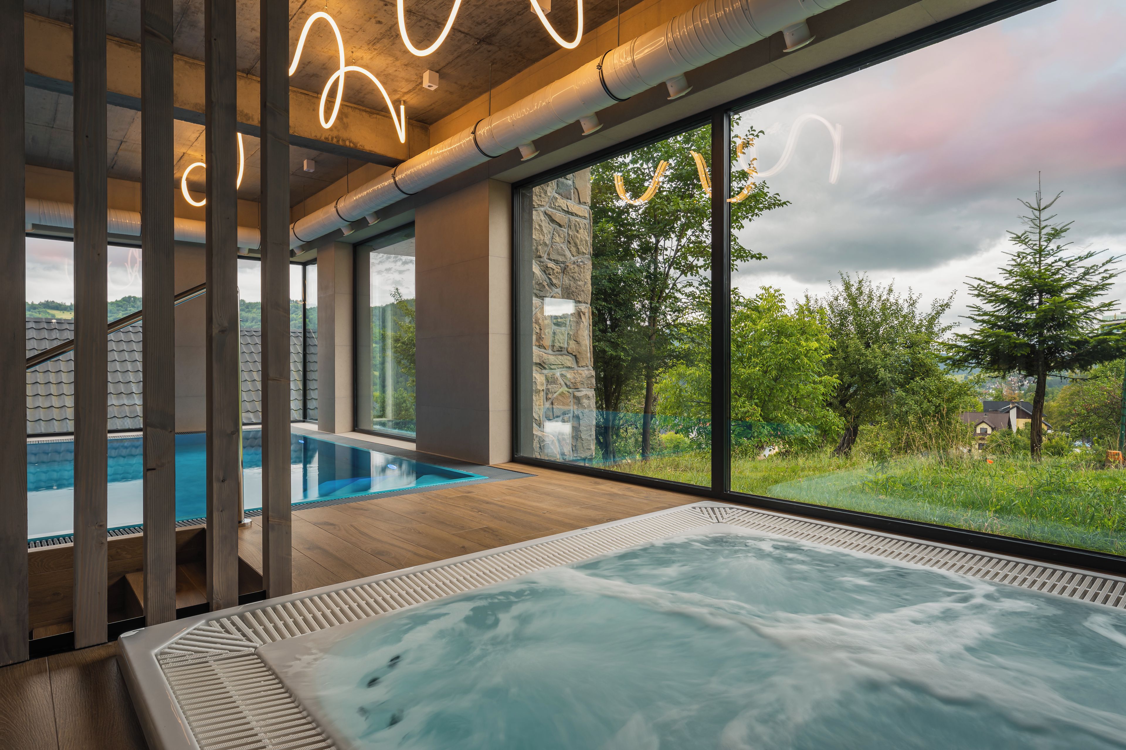 Ett modernt inomhuspoolområde med bubbelpool, stora fönster och utsikt över det omgivande landskapet.