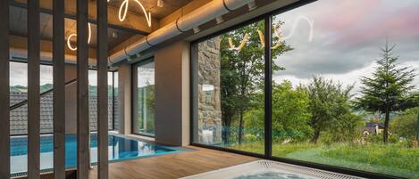 Un área de piscina interior moderna con un jacuzzi, amplios ventanales y vistas del paisaje circundante.