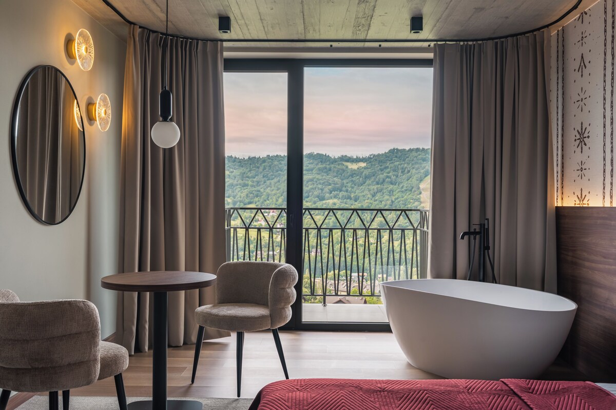 Un baño moderno con una bañera independiente, una mesa redonda, dos sillas y un amplio ventanal con vistas panorámicas.