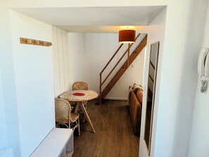 Ein kleiner Raum mit einer Holztreppe, einem runden Tisch mit Stühlen und einer Lampe.