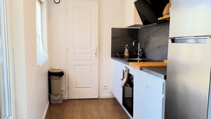 Kompakti keittiö, jossa on valkoiset kaapit, ruostumattomasta teräksestä valmistettu jääkaappi, sisäänrakennettu uuni ja pieni työtaso.
