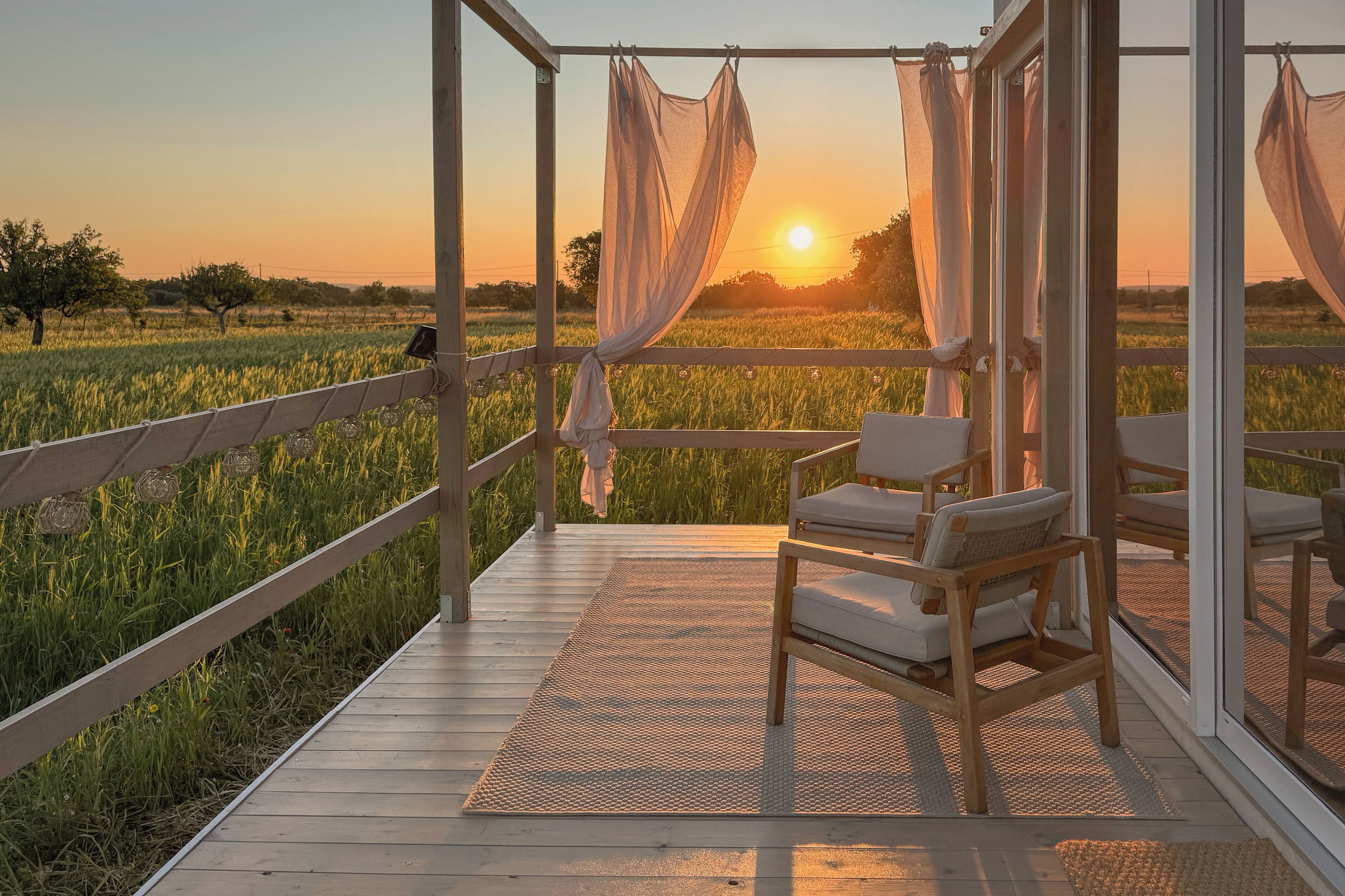 En træterrasse med udsigt over en solnedgang over et mark, en stol og et markise.