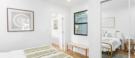 Un dormitorio con cama, una banca, un espejo y una ventana.