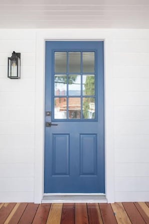 A blue door with a glass panel, a doorbell, and a wall-mounted light fixture. - The Vina {B} - A Coastal Downtown SB Retreat (Santa Barbara)