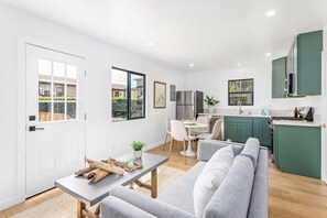 Eine moderne Küche mit grünen Schränken, ein Essbereich mit einem grauen Sofa und einer weißen Tür.