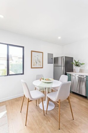 A modern kitchen with a stainless steel refrigerator, a dining table with four chairs, and a potted plant on the counter. - The Vina {B} - A Coastal Downtown SB Retreat (Santa Barbara)