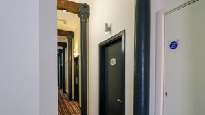 Un pasillo con puertas numeradas, un letrero de puerta corta fuegos y una cámara de seguridad.