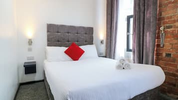 Una cama bien hecha con sábanas blancas, una almohada roja y toallas enrolladas a un lado.