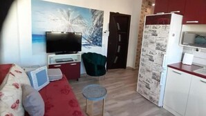 A compact living space with a sofa, a television, a small table, a kitchen area, and a door leading to another room. - Cozy 1-bedroom apartment in gorgeous Constanta with AC (Constanta)