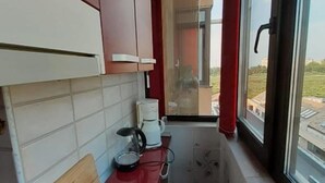 A narrow kitchen with red countertops, a coffee maker, and a window overlooking a building. - Cozy 1-bedroom apartment in gorgeous Constanta with AC (Constanta)