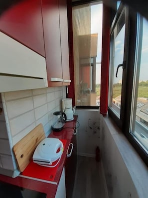 A narrow kitchen with red countertops, a coffee maker, and a window overlooking a building. - Cozy 1-bedroom apartment in gorgeous Constanta with AC (Constanta)