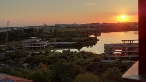 A sunset view from a balcony overlooking a body of water, with buildings and greenery in the foreground. - Cozy 1-bedroom apartment in gorgeous Constanta with AC (Constanta)