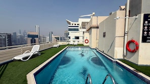 Ein Pool auf dem Dach mit Blick auf die Stadt, weißen Liegestühlen und einem Rettungsring.