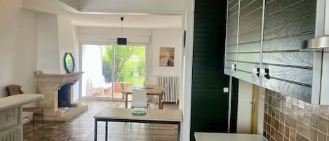 A spacious kitchen with a dining area, a fireplace, and a view of greenery outside.