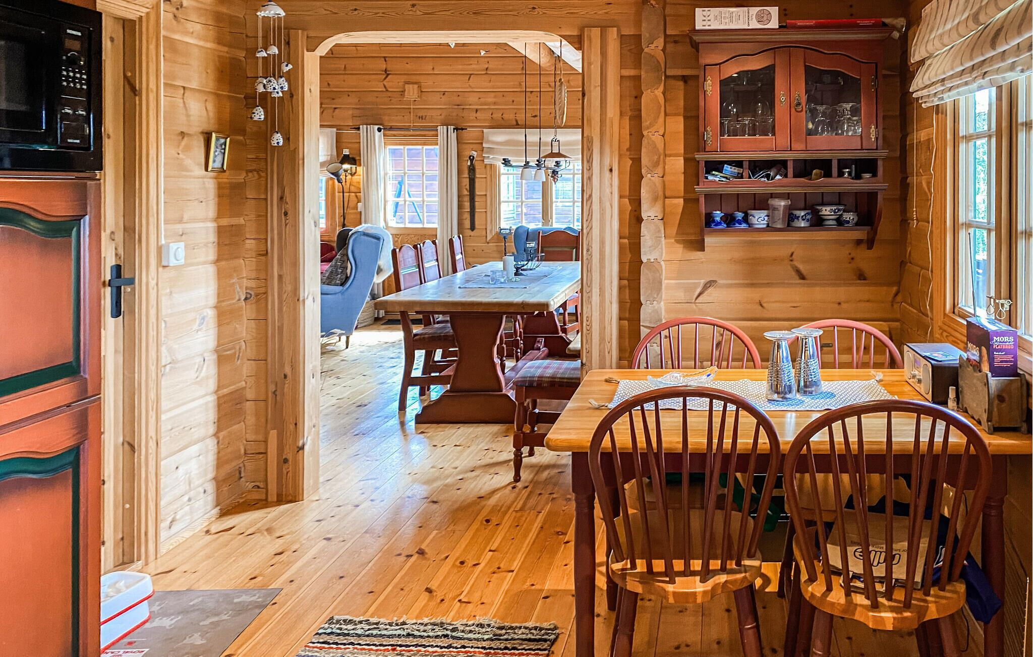 A wooden interior with a dining area, chairs, a table, and a cabinet with glass doors.