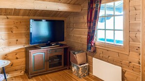 A wooden cabin interior with a television on a cabinet, a small table, and a window with curtains. - Stunning home in Bjorli with WiFi (Bjorli)