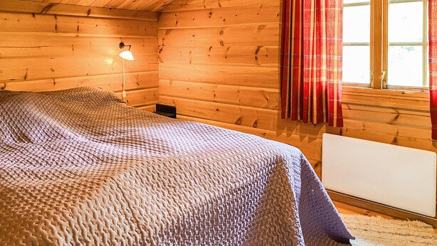 A wooden cabin room with a bed, a nightstand, a lamp, and a window with curtains. - Stunning home in Bjorli with WiFi (Bjorli)